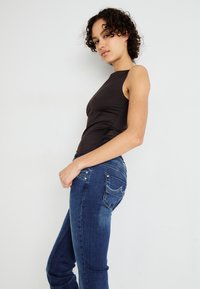 Top negro sin mangas con un escote alto, combinado con jeans de mezclilla ajustados de color azul que cuentan con bolsillos traseros y detalles de costura sutiles.