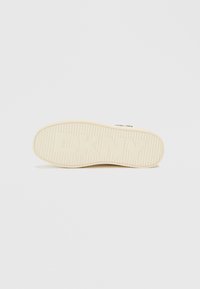 Ελαφρώς μπεζ σόλα αθλητικού παπουτσιού με ραβδωτή υφή και έντονο λογότυπο "DKNY", επίπεδο σχέδιο και στρογγυλεμένη άκρη. Λείο λάστιχο.