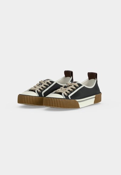 Μαύρα sneakers χαμηλού ύψους με μπεζ κορδόνια, λευκές προστασίες στα δάχτυλα, ανάγλυφες καφέ σόλες και καφέ λουριά στην φτέρνα, εμφανιζόμενα σε απλό λευκό φόντο.