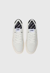 Sneakers din piele albă cu design perforat, căptușeală din textil negru cu logo și talpă din cauciuc bej. Stil clasic cu șireturi.