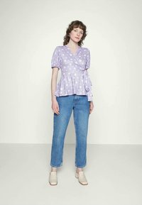 Top envolvente lavanda com padrões de estrelas brancas, mangas bufantes e um laço na cintura, combinado com jeans azuis de cintura alta e sapatos claros.