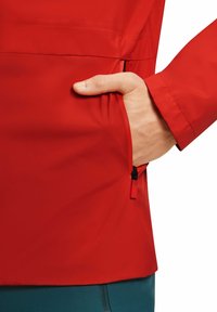 Giacca impermeabile rossa con una tasca laterale dotata di zip nera. Il tessuto ha una texture liscia e un design aderente.