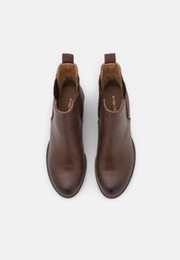 Bottes de cheville en cuir marron avec une texture lisse, bout rond, panneaux latéraux élastiques et languettes pour un enfilage facile.