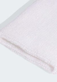 Tissu blanc texturé, doux et duveteux, avec un bord replié. Le matériau semble épais et moelleux, adapté pour la chaleur ou le confort.