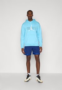 Svetlomodrá mikina s kapucňou a predným kengurím vreckom, so:bielym logom Jordan. V kombinácii s námorníckymi šortkami s modrými pruhmi a športovými topánkami.