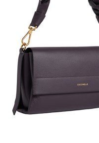 Borsa a tracolla in pelle testurizzata di colore viola scuro con chiusura in tonalità oro e logo "COCCINELLE" sulla pattina frontale.