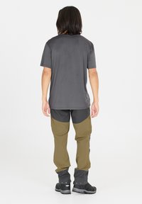 Grå kortärmad skjorta med rund halsringning, tillsammans med olivgröna och svarta byxor med böjda färgblock och elastiska mudd. Svarta vandringsskor.