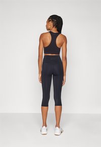 Černá sportovní podprsenka s racerback designem, spárovaná s černými legínami ke kotníkům. Hladký povrch, elastický materiál a délka ke kotníkům.