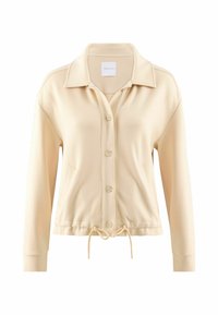 Giacca beige con zip realizzata in tessuto morbido. Presenta un colletto, chiusura con bottoni e vita regolabile con cordino. Maniche lunghe.