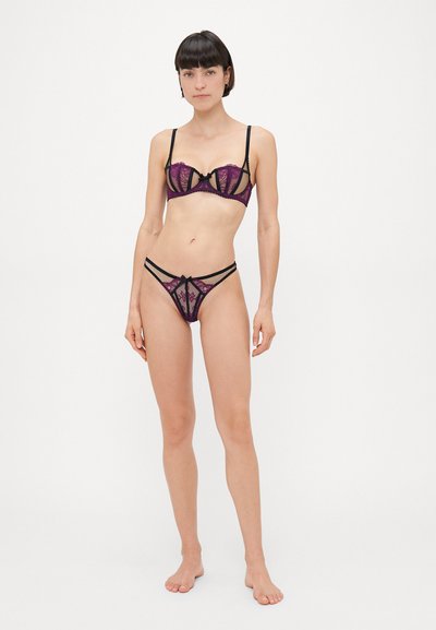 Set di lingerie in pizzo con una combinazione di colori viola e nero. Il reggiseno ha un design strutturato con pannelli trasparenti, spalline sottili e dettagli a fiocco.