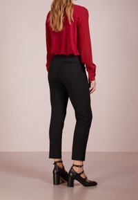 Červená halenka s dlouhým rukávem v kombinaci s černými smokinkovými kalhotami a černými lodičkami se sponovými detaily. Hladká tkanina s přiléhavým střihem.