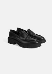 Zwarte leren loafers met een chunky, gestructureerde zool en een zachte, brede band over de voorkant. Gladde afwerking met een ronde teen design.