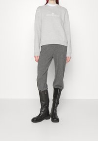 Šedá mikina s bílým logem, spárovaná se šedými tepláky a černými koženými botami až po kolena, s hladkou texturou a uvolněným střihem.