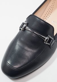 Mocassins en cuir noir à texture lisse. Dotés d'un accent en métal argenté sur le dessus, d'une forme à bout pointu et de détails de couture.
