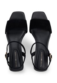 Μαύρα σανδάλια από σουέτ με χοντρό τακούνι, τετράγωνη μύτη, ρυθμιζόμενο λουράκι στον αστράγαλο και χρυσαφί μεταλλικά στοιχεία. Μαύρος λείος πάτος, μίνιμαλ σχεδιασμός.