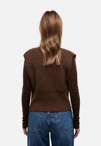 Pull tricoté marron avec une texture côtelée, design à épaules courtes et manches ajustées, associé à un jean bleu taille haute.