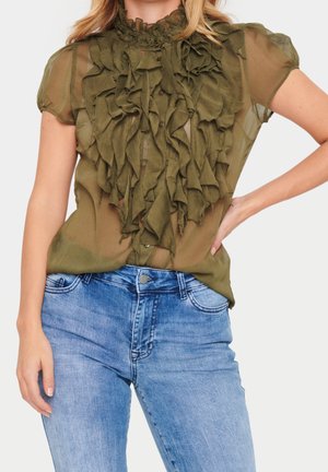 Olivengrøn gennemsigtig bluse med flæsedetaljer foran, korte puffede ærmer, kombineret med lyseblå højttaljede denimjeans.