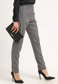 Pantaloni grigi su misura con una texture liscia, dotati di tasche laterali, una vestibilità slim, abbinati a tacchi a spillo neri e una borsa a mano.