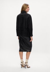 Blusa preta com barra de renda floral, combinada com uma saia de couro preta. Modelo a usar sapatos de salto com tiras e meias até ao joelho.