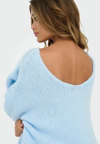 Jasnoniebieski sweter z dzianiny o otwartym plecach, miękka tekstura, prążkowane krawędzie i luźny krój, z lekko oversize'ową sylwetką.