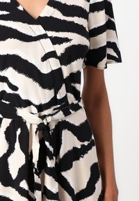 Šaty s překřížením v černé a krémové barvě, s designem zebřího vzoru, krátkými rukávy, výstřihem do V a odpovídajícím zavazovacím páskem v pase.