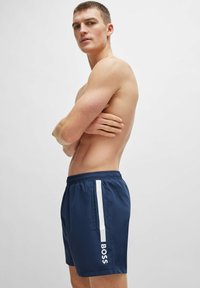 Ναυτικά σορτς κολύμβησης με λευκή ρίγα και λογότυπο στο πλάι, ελαστική μέση, λεία υφή και κλασική εφαρμογή.