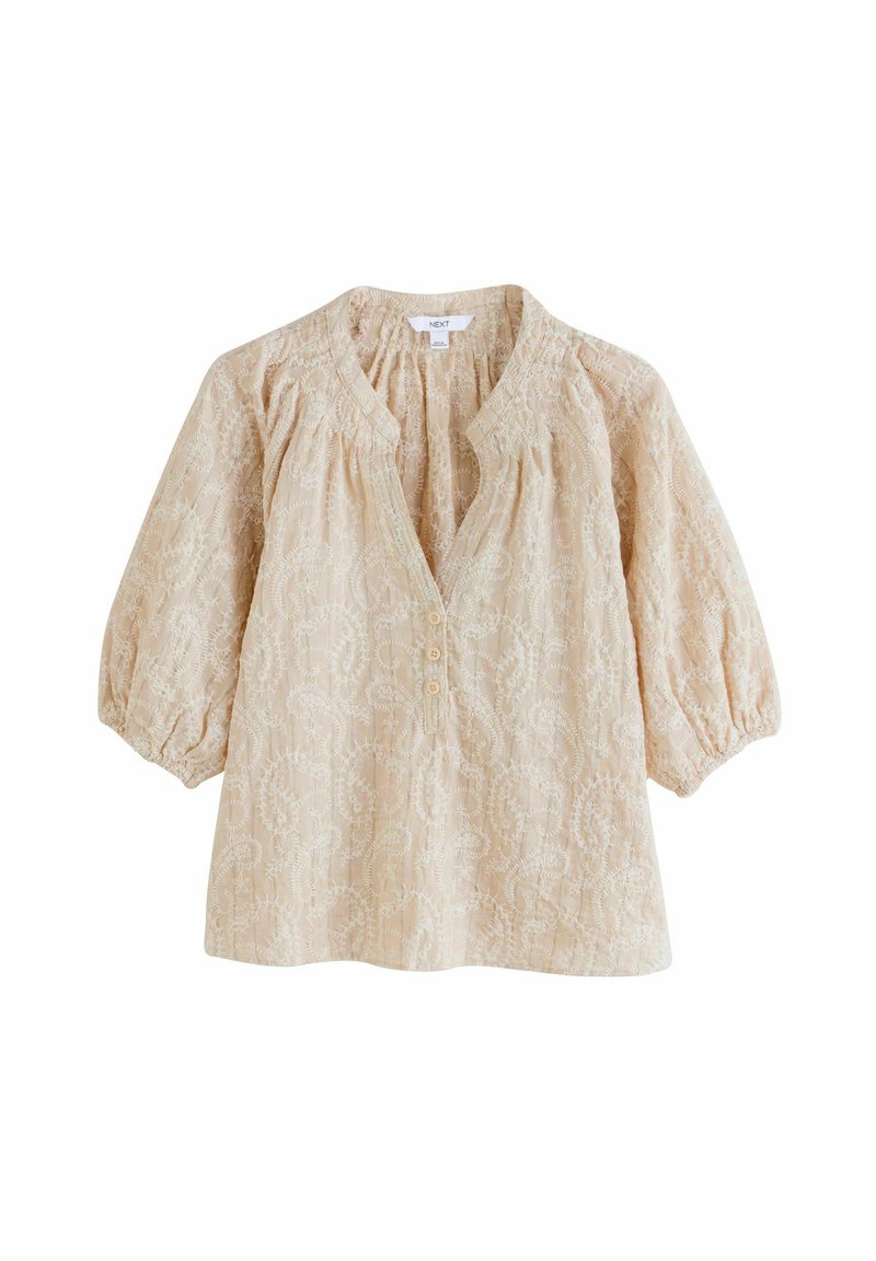 Blusa beige claro con un patrón floral, escote en V, tapeta de botones y mangas abullonadas. Tejido texturizado con delicados bordados.