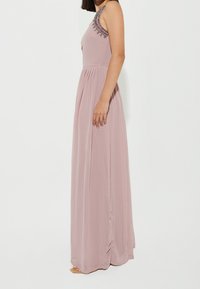 Robe maxi en tissu mauve doux avec un corsage ajusté, une jupe plissée, et des détails de bretelle ornés. Texture lisse, design sans manches.