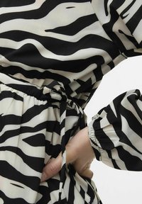 Robe en imprimé zèbre noir et blanc avec une taille cintrée à nouer, manches longues avec des poignets élastiques et une texture de tissu fluide.