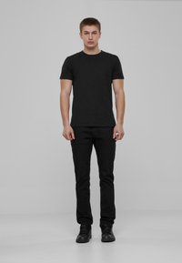 Crna majica kratkih rukava u kombinaciji s crnim uskim hlačama i crnim visokim tenisicama. Outfit ima jednostavan, minimalistički dizajn.
