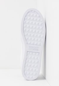 Semelle de sneaker en caoutchouc blanc avec un motif en diamant surélevé. Présente un marquage "TOMMY JEANS", des bords arrondis, une texture lisse et un design minimaliste.