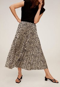 Gonna maxi a stampa nera e beige con un design fluente, caratterizzata da una lunghezza fino al polpaccio e un tessuto leggero. Abbinata a un top nero e sandali.