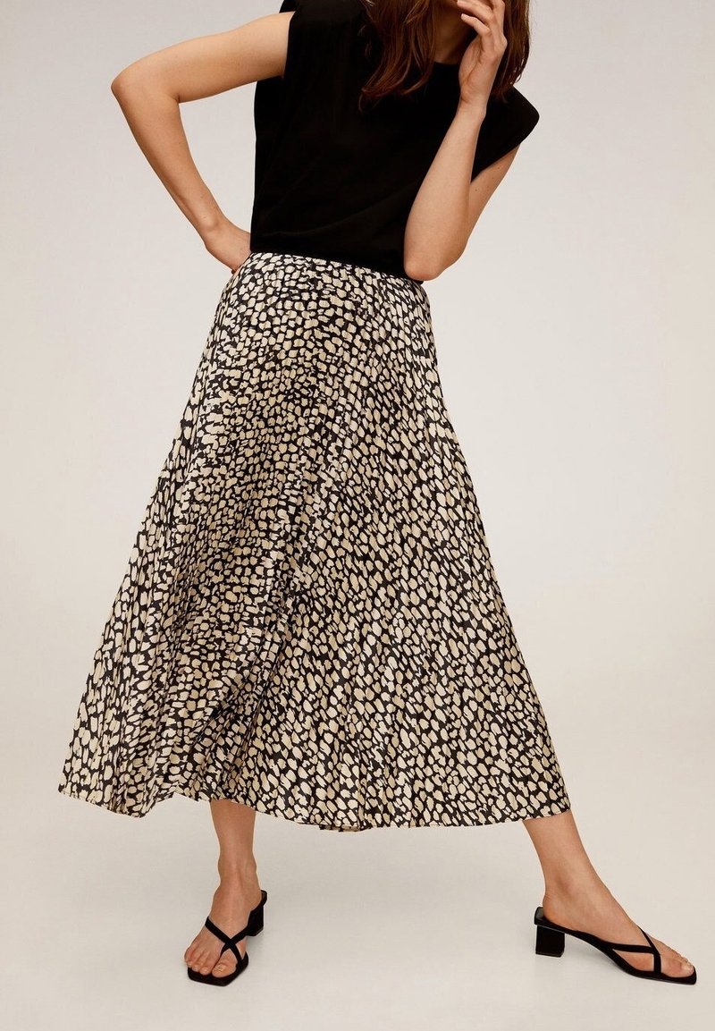 Gonna maxi a stampa nera e beige con un design fluente, caratterizzata da una lunghezza fino al polpaccio e un tessuto leggero. Abbinata a un top nero e sandali.
