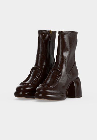 Paire de bottines en cuir marron foncé brillant avec talons carrés et fermetures éclair sur le côté, avec un motif en relief distinct sur le devant.