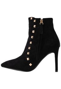 Bottine en daim noir à bout pointu, ornée de clous pyramides dorés sur le côté et équipée d'une fermeture éclair latérale. Talon aiguille.