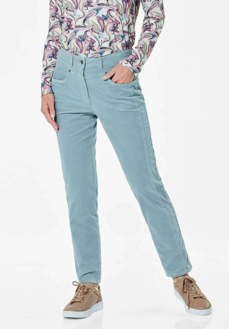Lichtblauwe corduroy broek met voorkruiszakken en een aansluitend ontwerp, gecombineerd met tan sneakers. De stof heeft een zachte textuur.