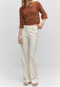 Maglione marrone corto in maglia con motivi testurizzati e maniche arricciate abbinato a pantaloni bianchi a vita alta e a gamba larga.