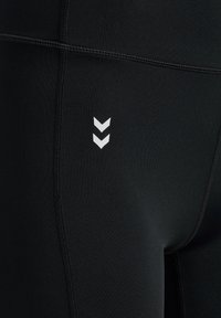 Czarne legginsy sportowe o gładkiej fakturze, z białymi wzorami w zygzak i kontrastującymi detalami szycia.