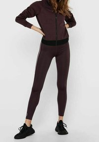 Vínová sportovní bunda s černými akcenty, na zip a s dlouhými rukávy, spárovaná s odpovídajícími vínovými legínami a černými teniskami.