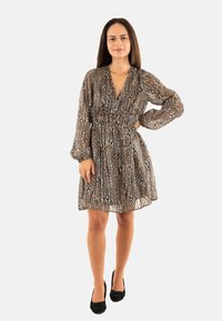 Robe à motif floral en marron et beige, avec des manches longues, une taille cintrée et un décolleté en V, assortie à des chaussures noires. Texture de tissu lisse.