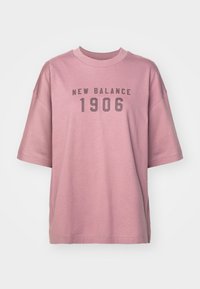 Roza velikanska majica iz bombaža, s kratkimi rokavi. Sprednji dizajn vključuje "NEW BALANCE 1906" v sivi barvi. Gladka tekstura.