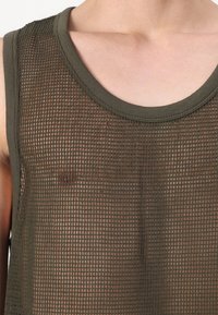 Close-up of a person wearing a sleeveless dark green mesh top revealing bare chest underneath.