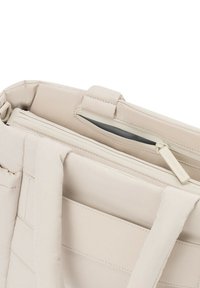 Sac beige matelassé avec des bretelles épaisses et une poche intérieure zippée, partiellement ouvert montrant une texture douce et matelassée.