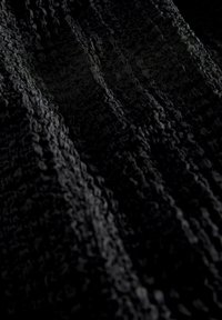 Tessuto nero con una trama texturizzata e un motivo ondulato, caratterizzato da una superficie morbida e stropicciata che riflette la luce in varie sfumature di scuro.