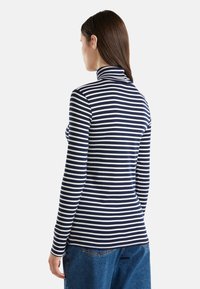 Langärmliger Rollkragenpullover in Marineblau und weißen Streifen, mit passgenauer Schnittform und weicher Textur, kombiniert mit lockeren blauen Jeans.