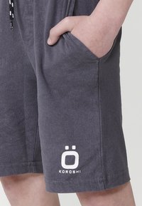 Sivé bavlnené šortky s elastickým pásom, bočnými vreckami a bielym logom s nápisom "KOROSHI" na prednej strane, ktoré ponúkajú hladký povrch.