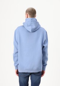 Lichtblauwe hoodie met een trekkoordkap, lange mouwen en ribgebreide manchetten. Soepele stof met een relaxed fit, gecombineerd met donkere jeans.