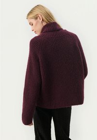 Bordeaux gebreide trui met hoge kraag, geribbelde textuur en oversized pasvorm. Heeft verlaagde schouders en een boxy silhouet.