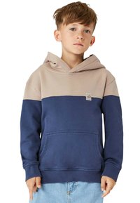 Hoodie i beige och marinblå. Har en kängeru ficka, ribbade ärmar och en tygpatch-logotyp på bröstet. Mjuk, strukturerad material.