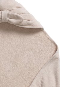Beige, mjukt tyg med en texturerad yta; har en knuten detalj vid kragen och en slät kant längs ena sidan.
